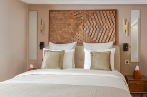 Een hotelkamer met een hoofdeinde van baksteenmotief, een bed met witte lakens, een nachtkastje met een zakdoos en een wandspiegel.
