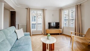 A living room with a sofa, a coffee table, a TV, and a chair. - Palais Royal - Prestige between the Louvre and the Opera (Paris)
