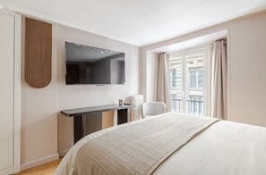 Hotelkamer met een bed, bureau, stoel, televisie en raam met gordijnen.