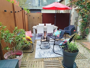 An outdoor patio with a table and chairs, a red umbrella, and potted plants.