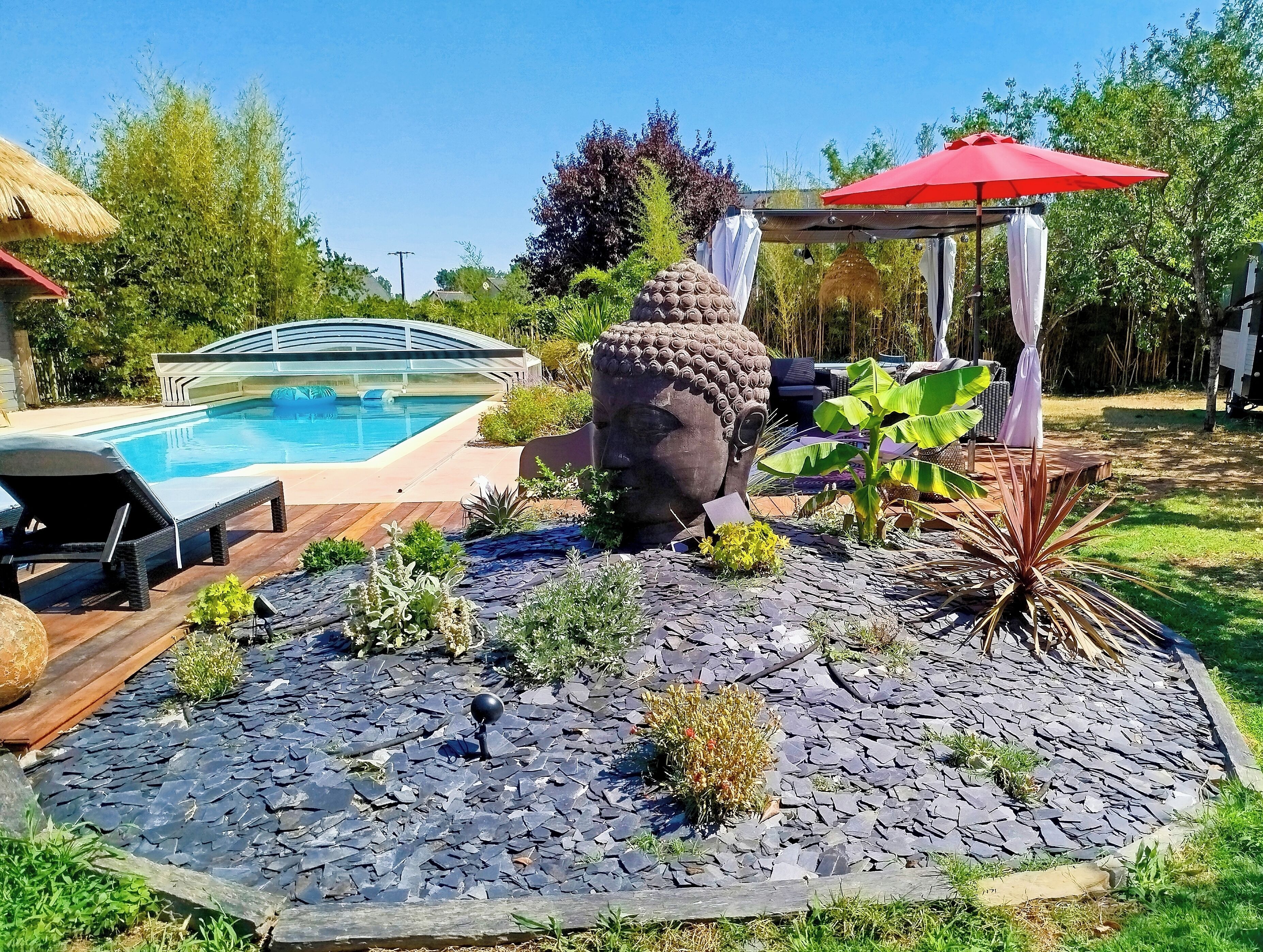 A swimming pool, a large decorative stone sculpture, a red umbrella, and a wooden deck.