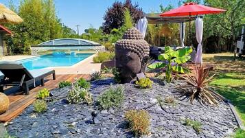 A swimming pool, a large decorative stone sculpture, a red umbrella, and a wooden deck.