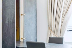 A modern room with a concrete wall, a wooden door, a curtain, and a table with chairs. - Knightsbridge 1Bed | Harrods (London)
