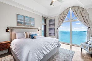 Ein Schlafzimmer mit einem großen Bett, einem Nachttisch, einem Sessel und Blick auf das Meer.
