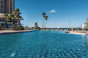 Ein Schwimmbad mit Liegestühlen und Palmen, umgeben von einem Gebäude mit Meerblick.