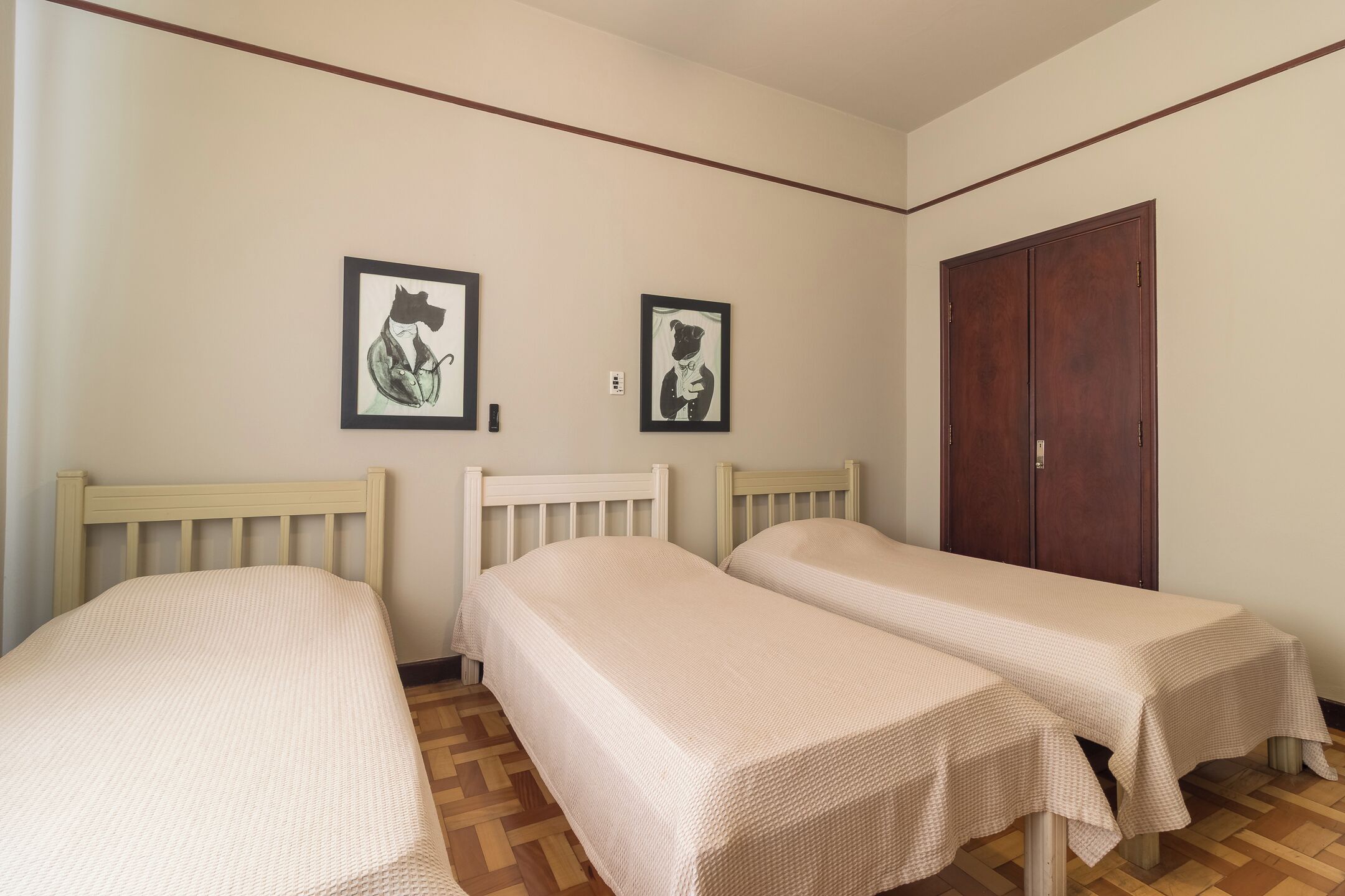 Una habitación con dos camas individuales, un armario y dos cuadros en la pared.