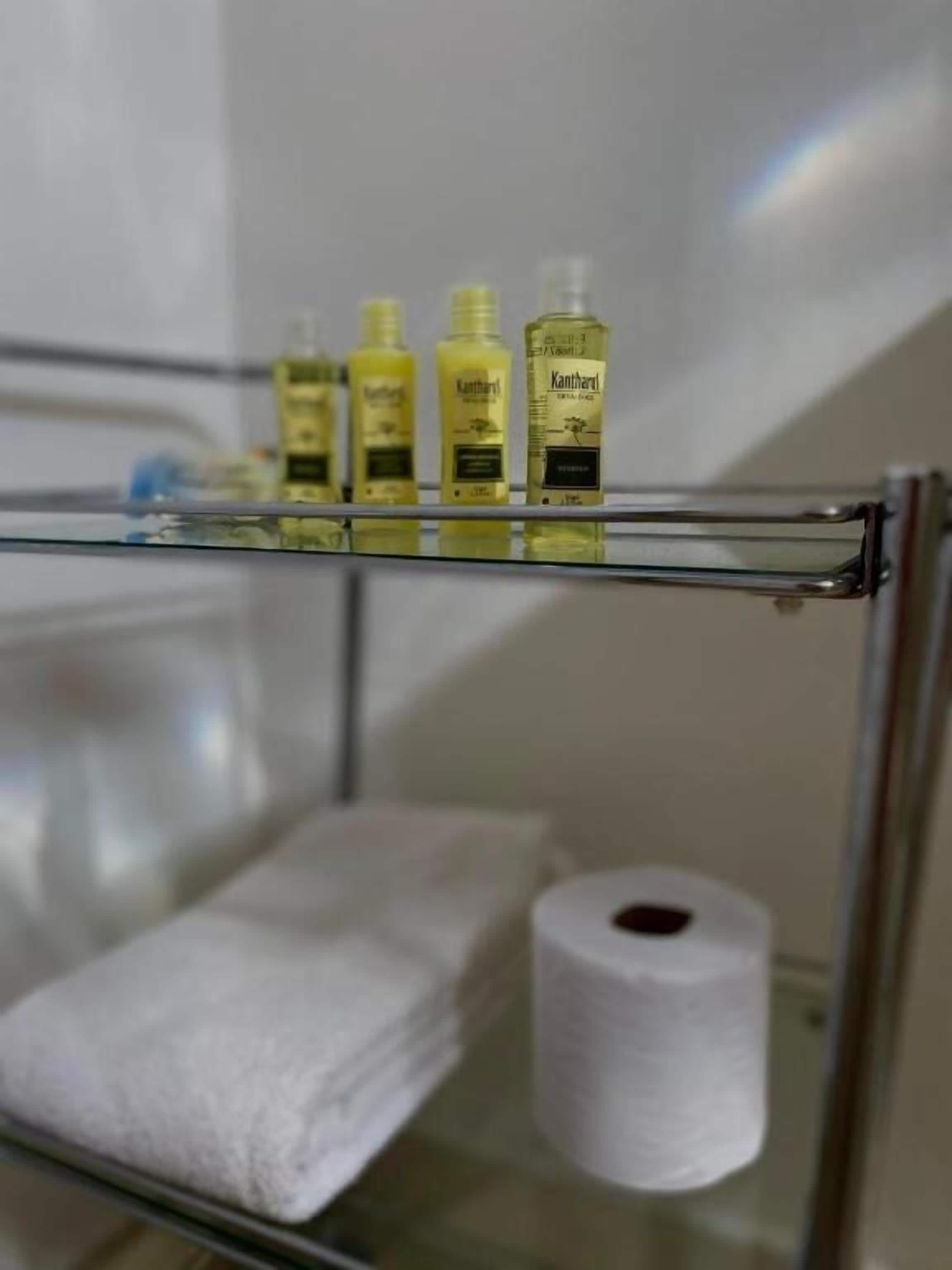 Een badkamer met een glazen plankje met toiletartikelen, een witte handdoek en een rol wc-papier.