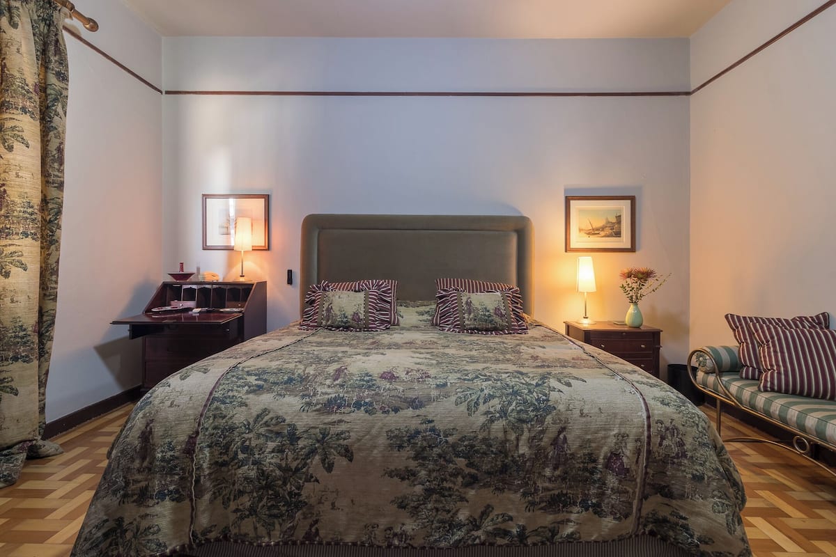 A bedroom with a large bed, two bedside tables, a nightstand, a sofa, and a wall-mounted lamp.