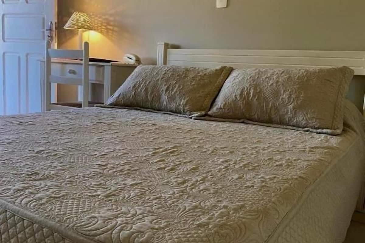 A bed with a quilted cover, a bedside table with a lamp, and a painting on the wall.