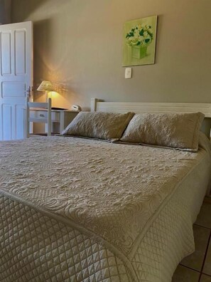 A bed with a quilted cover, a bedside table with a lamp, and a wall-mounted painting.