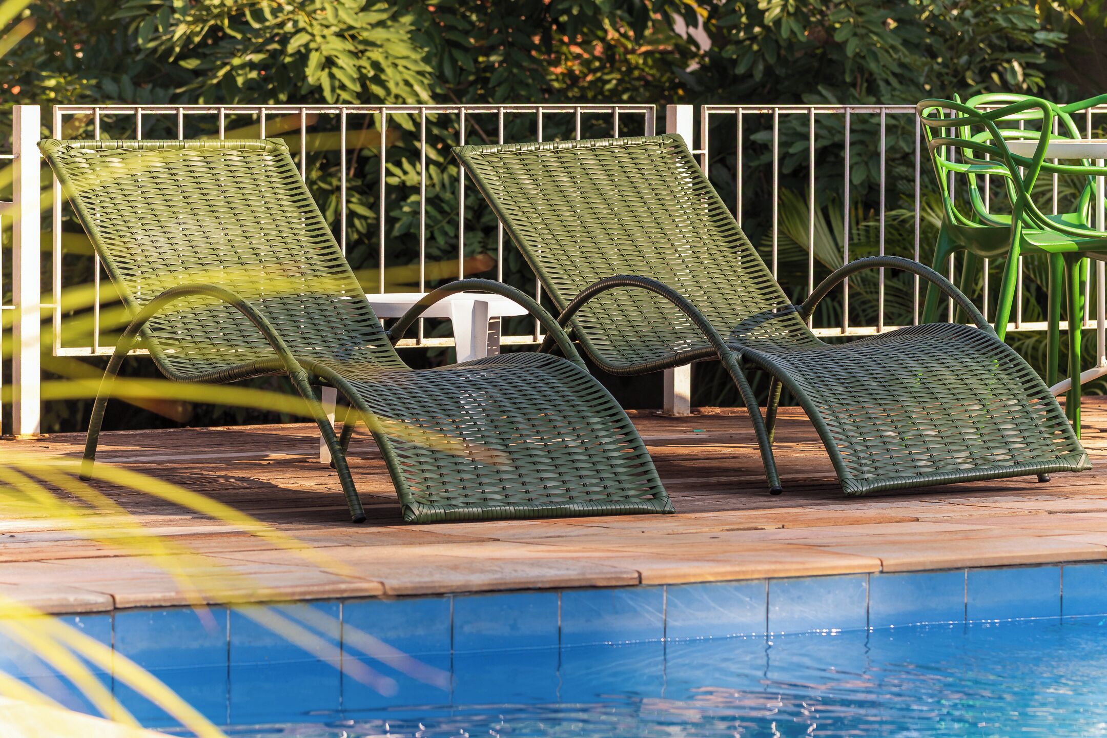 A poolside area with two green wicker lounge chairs and a white table.