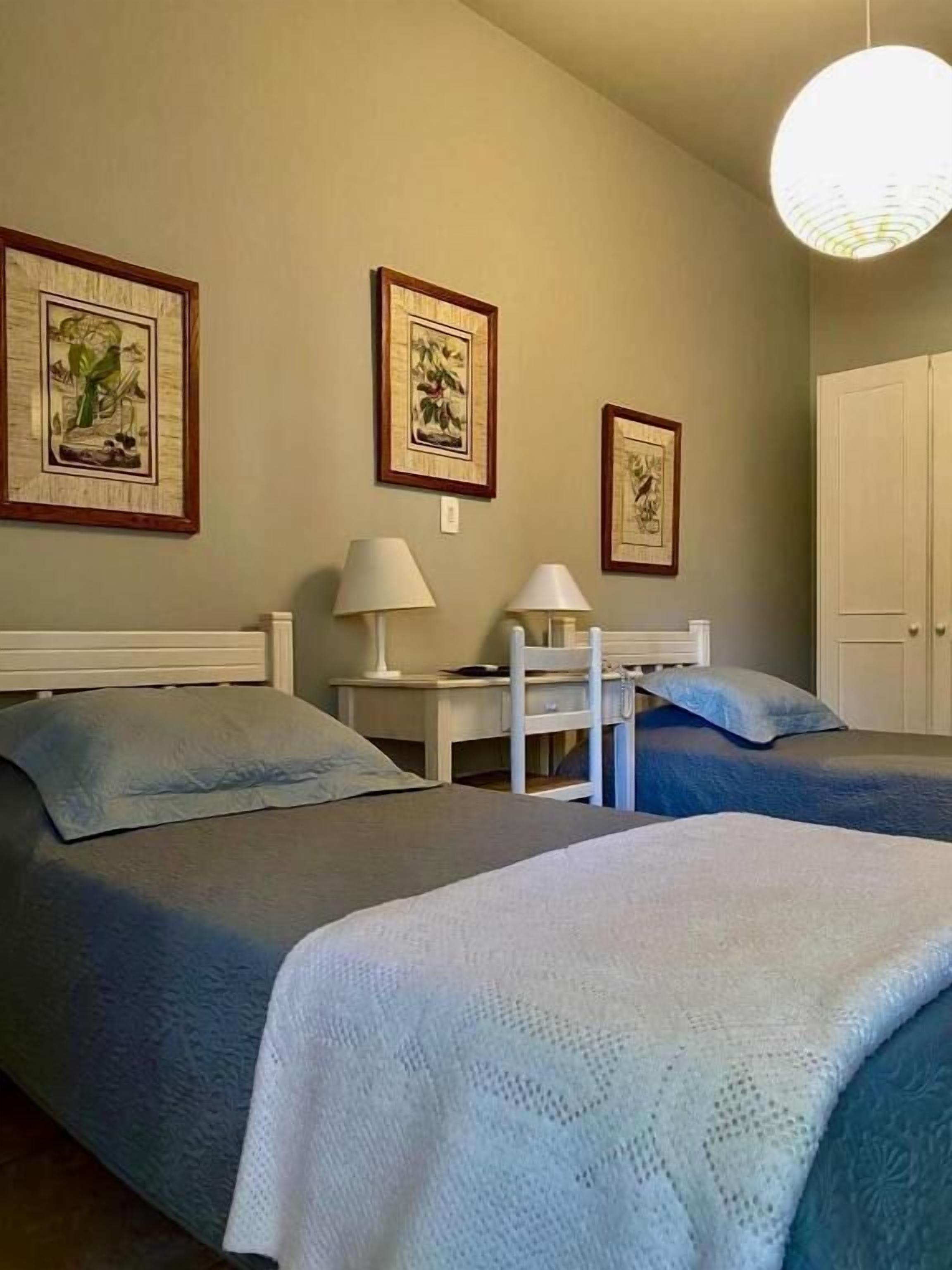 Een hotelkamer met twee bedden, een bureau, een stoel en ingelijste foto's aan de muur.
