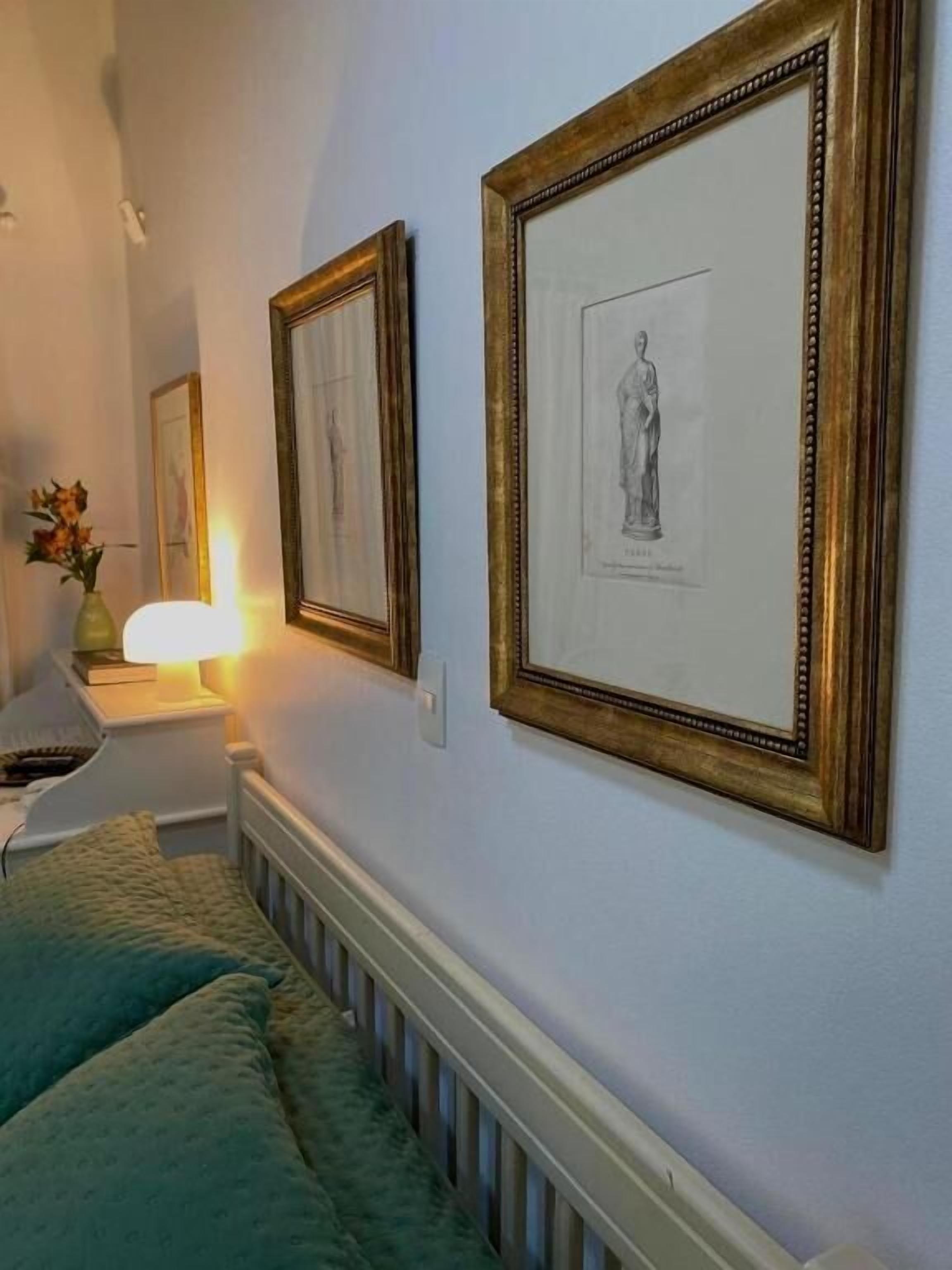 A room with a bed, a nightstand with a lamp, and framed artwork on the wall.