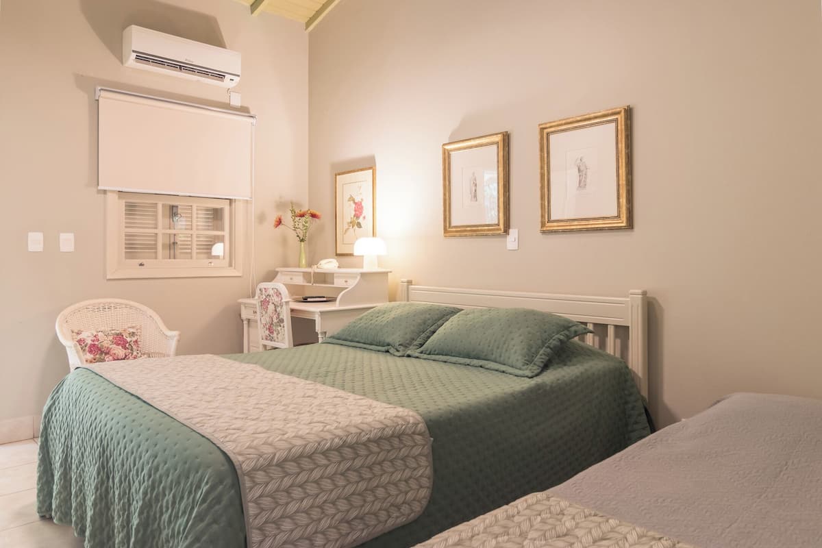 A bedroom with two beds, a desk, a chair, and framed pictures on the wall.