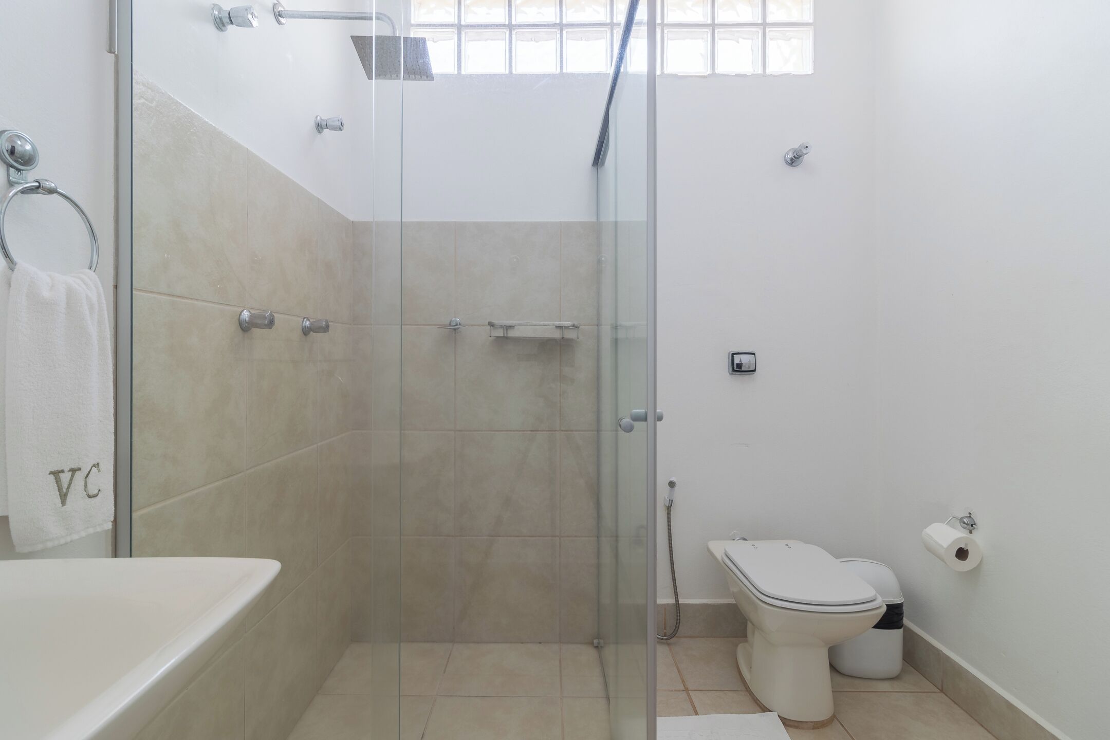 Un baño con ducha de vidrio, bañera blanca, inodoro y toallero con toalla.