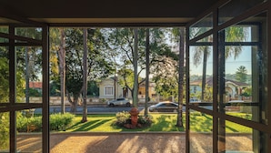 A view through a window with a paved area, a fire hydrant, and a street with cars and buildings in the background. - Pousada Villa do Conde (Brotas)