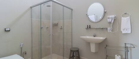 A modern bathroom with a glass-enclosed shower, a sink, a toilet, a hairdryer, and a towel rack.