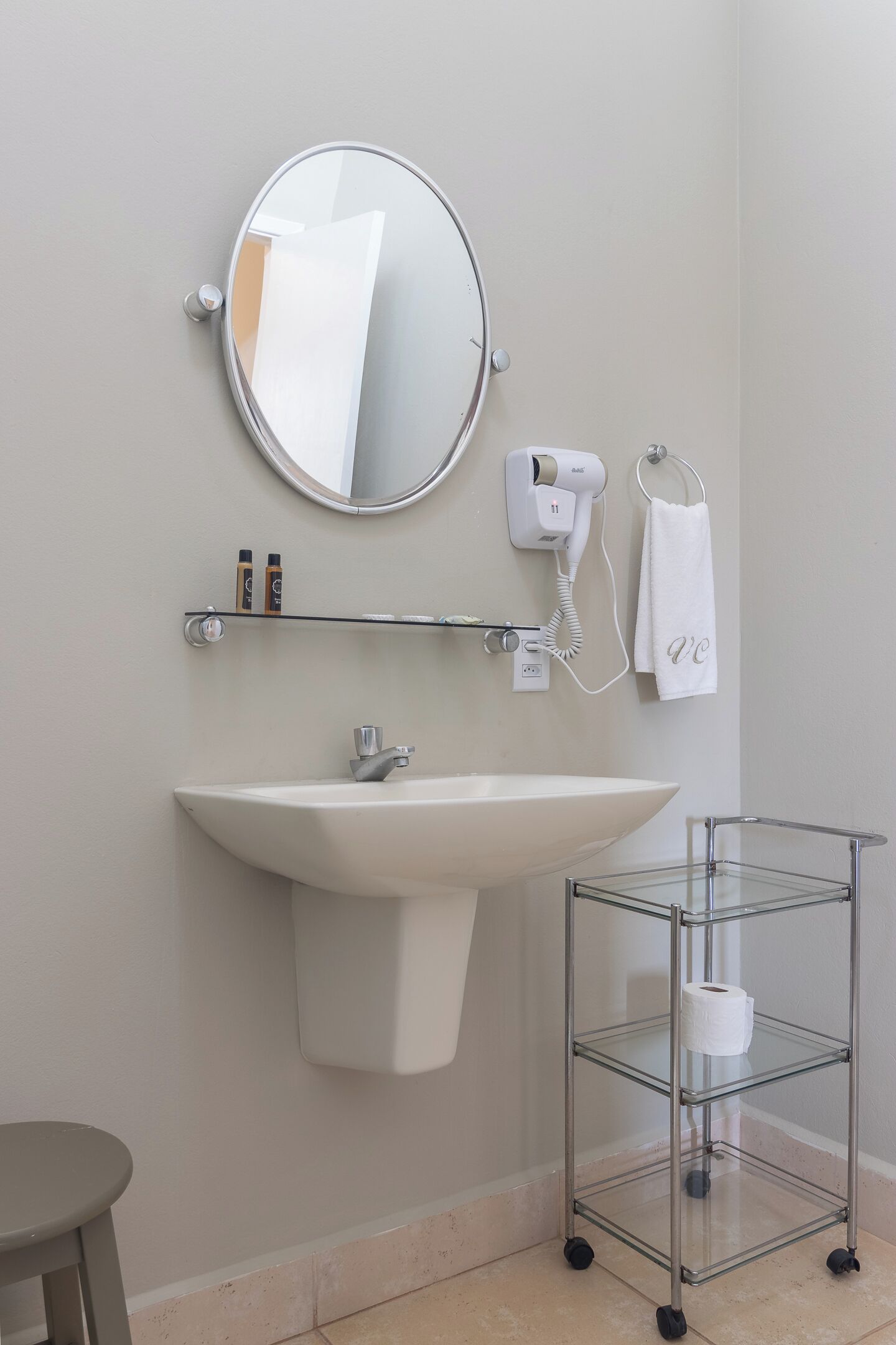 Une salle de bain équipée d’un lavabo, d’un miroir, d’un porte-serviettes, d’un sèche-cheveux et d’un présentoir en verre contenant un rouleau de papier toilette.