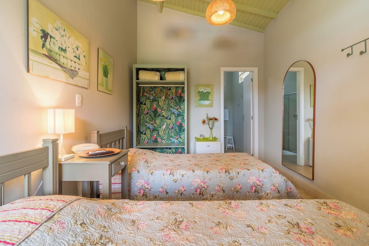 A bedroom with two beds, a desk, a chair, a lamp, a mirror, and artwork on the walls.