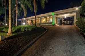 Un edificio con entrada pavimentada, fachada bien iluminada y letrero verde.