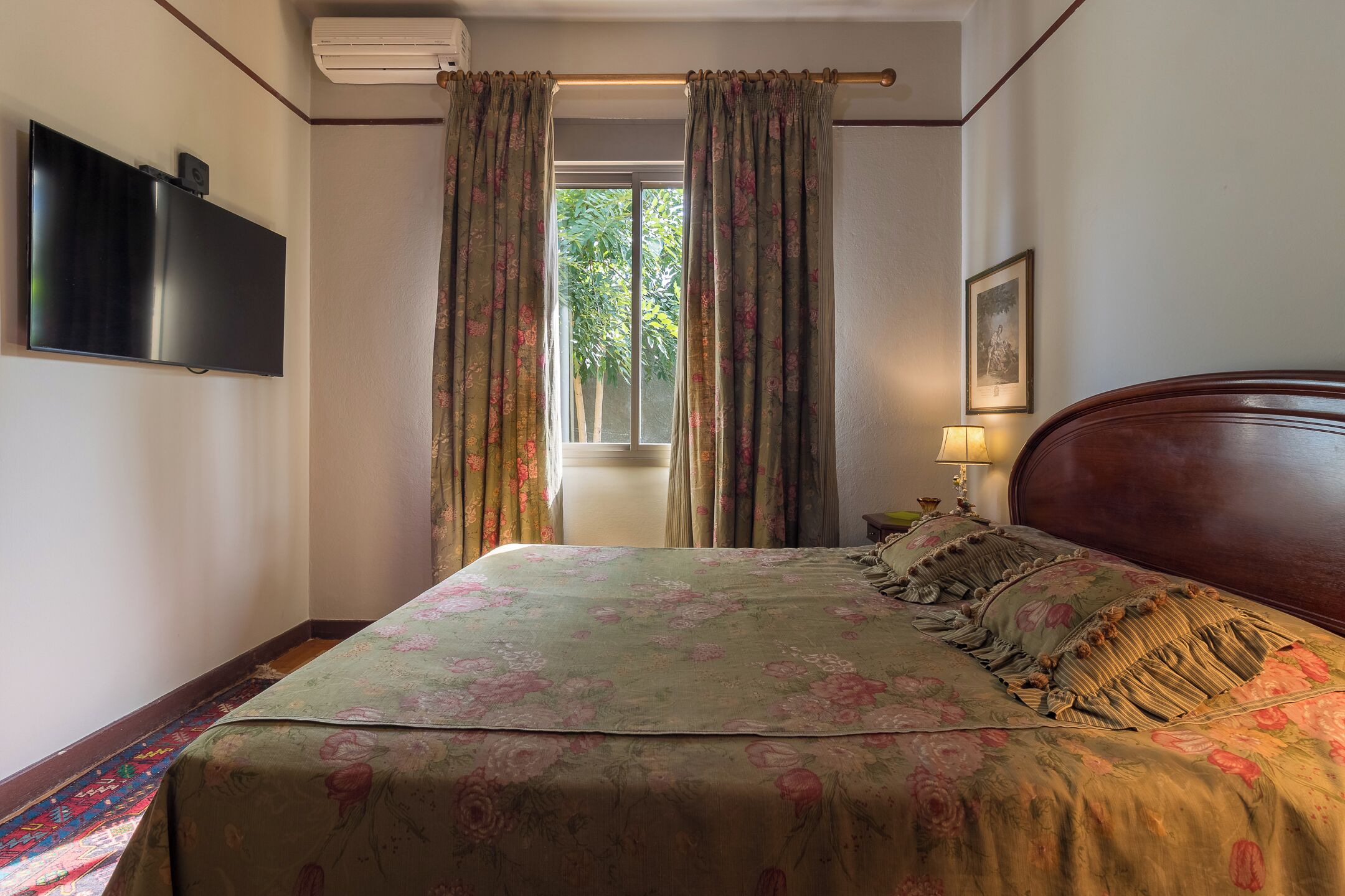 Een slaapkamer met een bed, gordijnen, een televisie, een lamp en een raam.