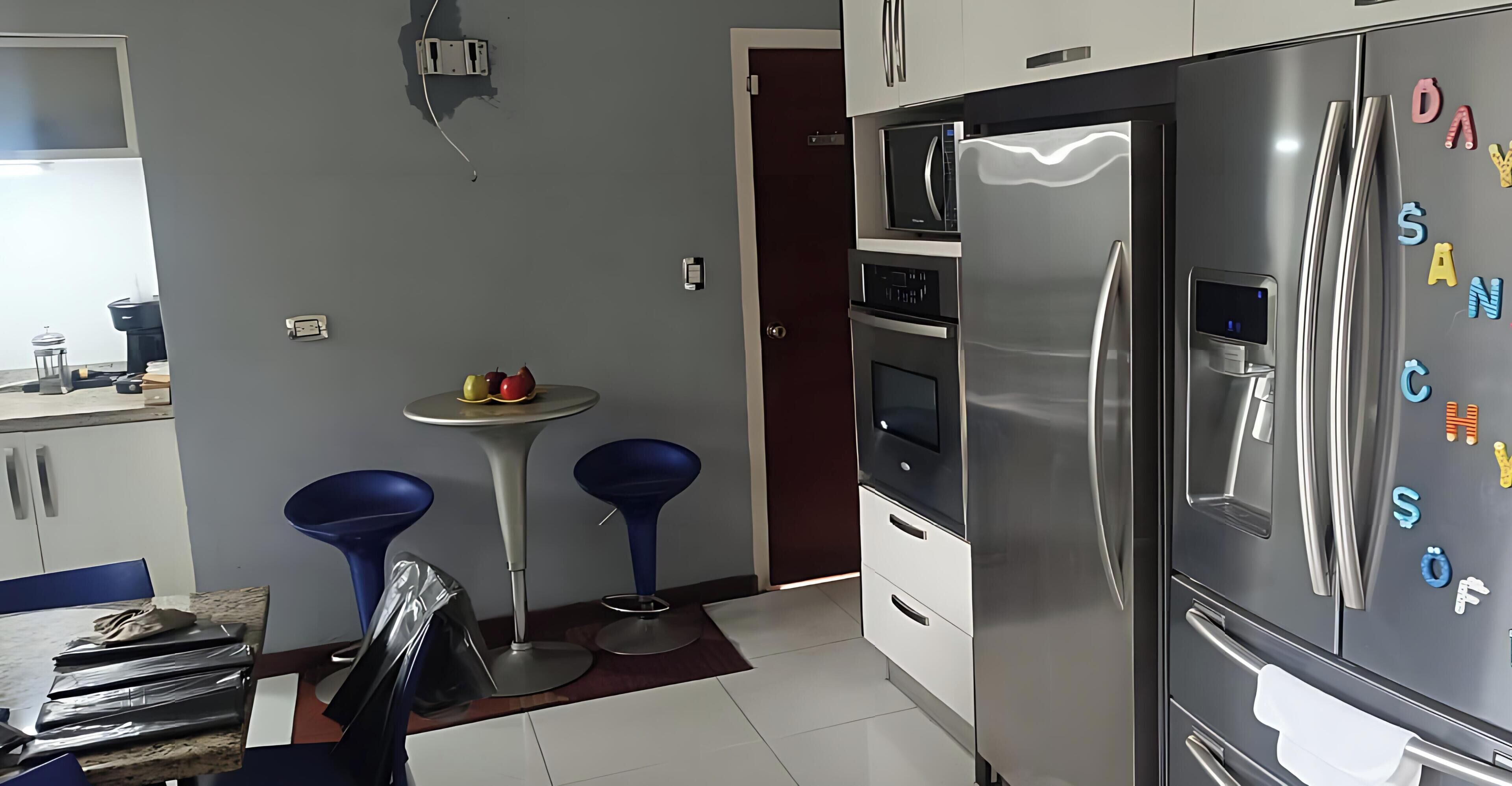 Une cuisine moderne équipée d’un réfrigérateur en acier inoxydable, d’un four à micro-ondes et d’une petite table avec des chaises.