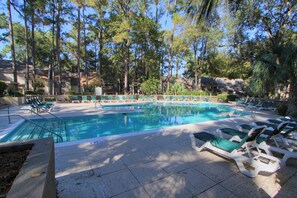 Ein Pool mit Liegestühlen und einer Steindeck, umgeben von Bäumen.