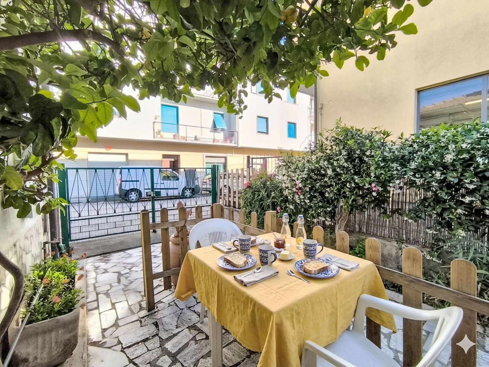 Eine Terrasse mit Tisch für zwei Personen, umgeben von einem Holzzaun und Grünpflanzen.