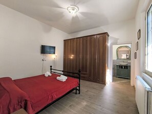 Ein Schlafzimmer mit einem Bett, einem Fernseher, einem Kleiderschrank und einem durch eine offene Tür einsehbaren Badezimmer.