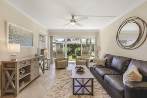 Ein Wohnzimmer mit einer Couch, Sesseln, einem Couchtisch, einem Deckenventilator und einem großen Fenster.