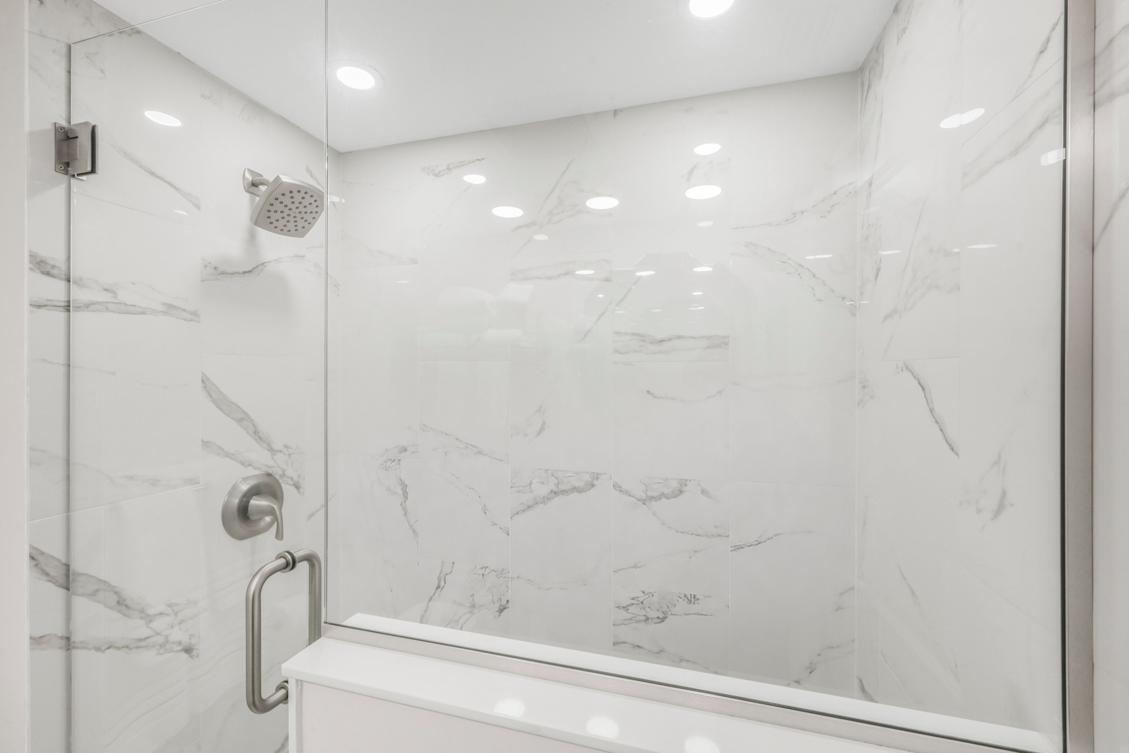 Eine moderne Dusche mit Duschbrause, Glastür und Wand in Marmoroptik.