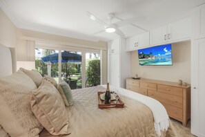 Ein Schlafzimmer mit Bett, Fernseher an der Wand, Deckenventilator und Blick ins Freie.