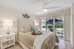 Ein Schlafzimmer mit einem Bett, Nachttischlampen, einem Deckenventilator und Blick ins Freie.