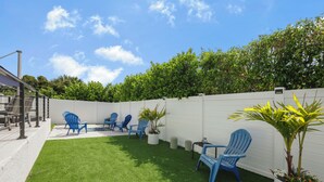 A backyard with artificial grass, blue Adirondack chairs, and potted plants. - Coastal Modern Home | Walk To Beach, Food & Shopping (Marco Island)