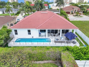 Une maison à deux étages avec un toit recouvert de tuiles rouges, une piscine et une terrasse aménagée avec du mobilier d’extérieur.