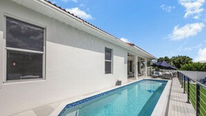 A swimming pool with a tiled edge, a white building with windows, and a clear sky. - Coastal Modern Home | Walk To Beach, Food & Shopping (Marco Island)