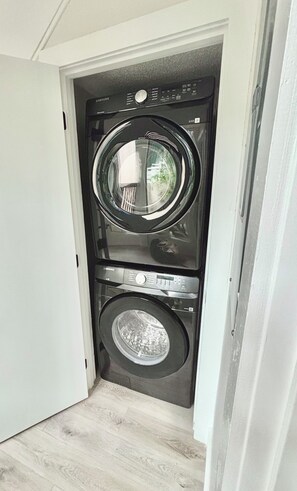 Ein kleiner Waschraum mit einer Waschmaschine und einem Trockner, einem Fenster und Holzboden.