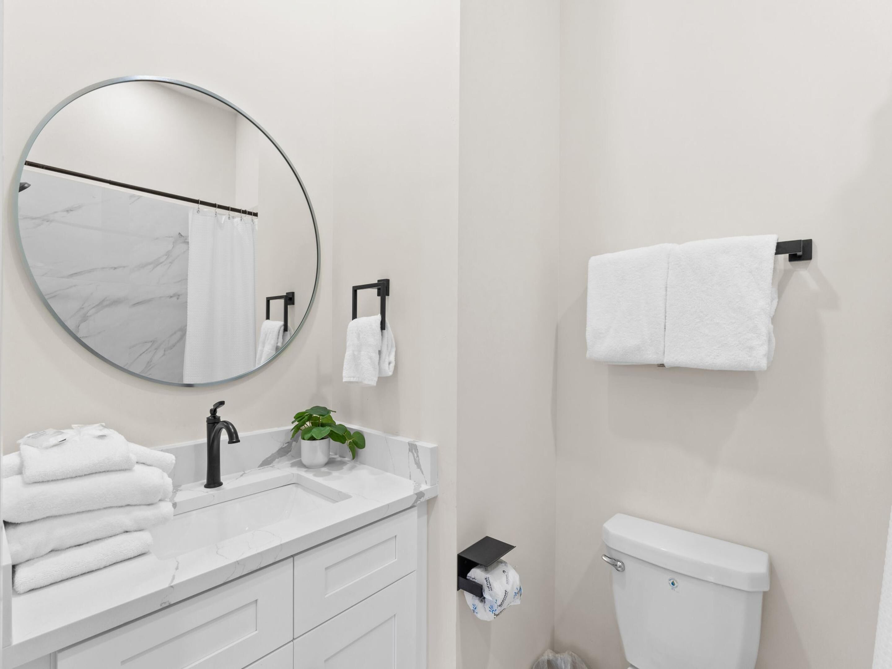 Ein modernes Badezimmer mit rundem Spiegel, weißem Marmorwaschtisch, Waschbecken, Toilette und Handtuchhalter.