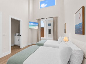 Ein Hotelzimmer mit zwei Betten, einem Fernseher, einem Fenster mit Vorhängen und einem Bild an der Wand.
