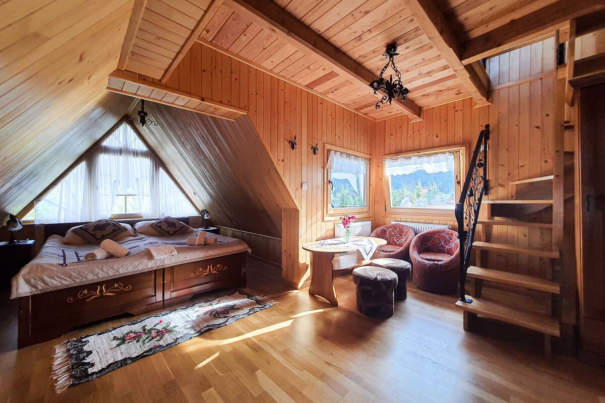 Una habitación de madera con una cama, una mesa, dos sillas, un radiador y una escalera.