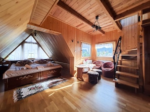 A wooden room with a bed, a table, two chairs, a radiator, and a staircase.