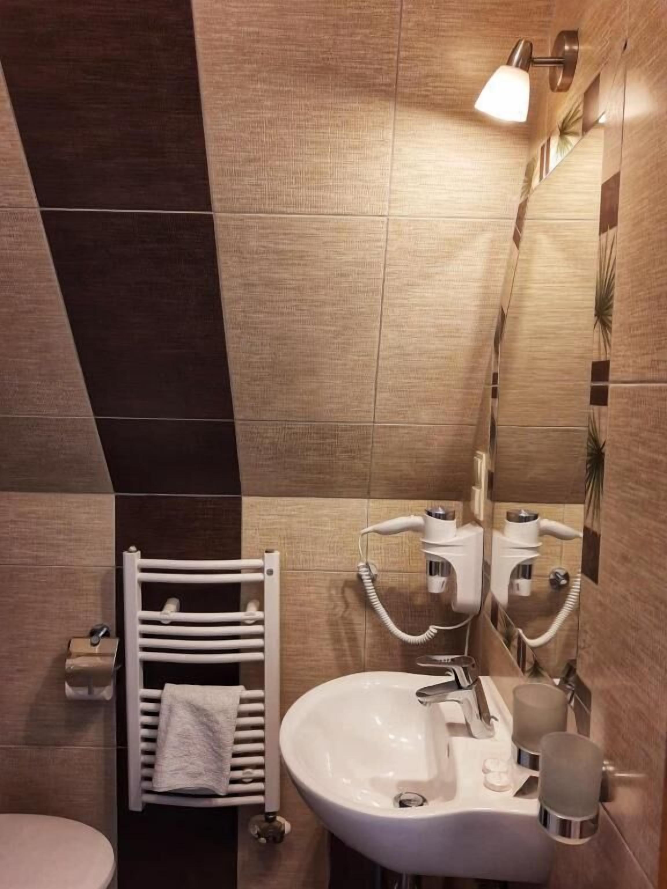 A bathroom with a white sink, a towel rack, a mirror, and a wall-mounted light fixture.