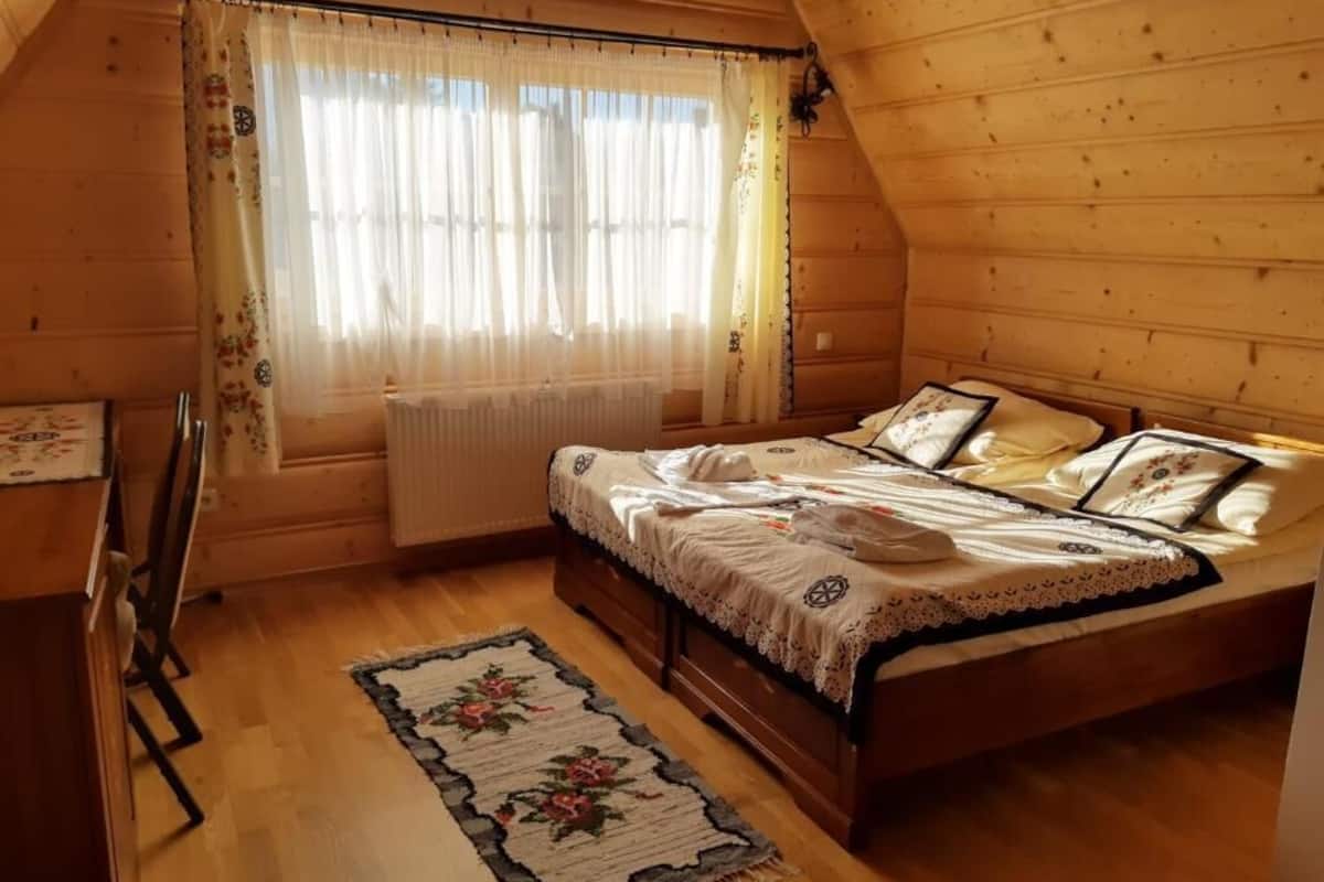 Un dormitorio acogedor de cabaña de madera, con cama, radiador y ventana con cortinas.
