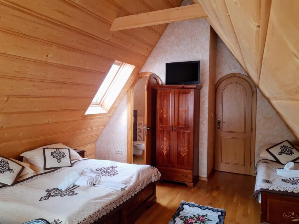 Un dormitorio con techo de madera, una cama con ropa de cama estampada, un armario, un televisor en la pared y una puerta.