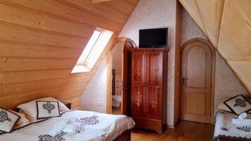 Un dormitorio con techo de madera, una cama con ropa de cama estampada, un armario, un televisor en la pared y una puerta.
