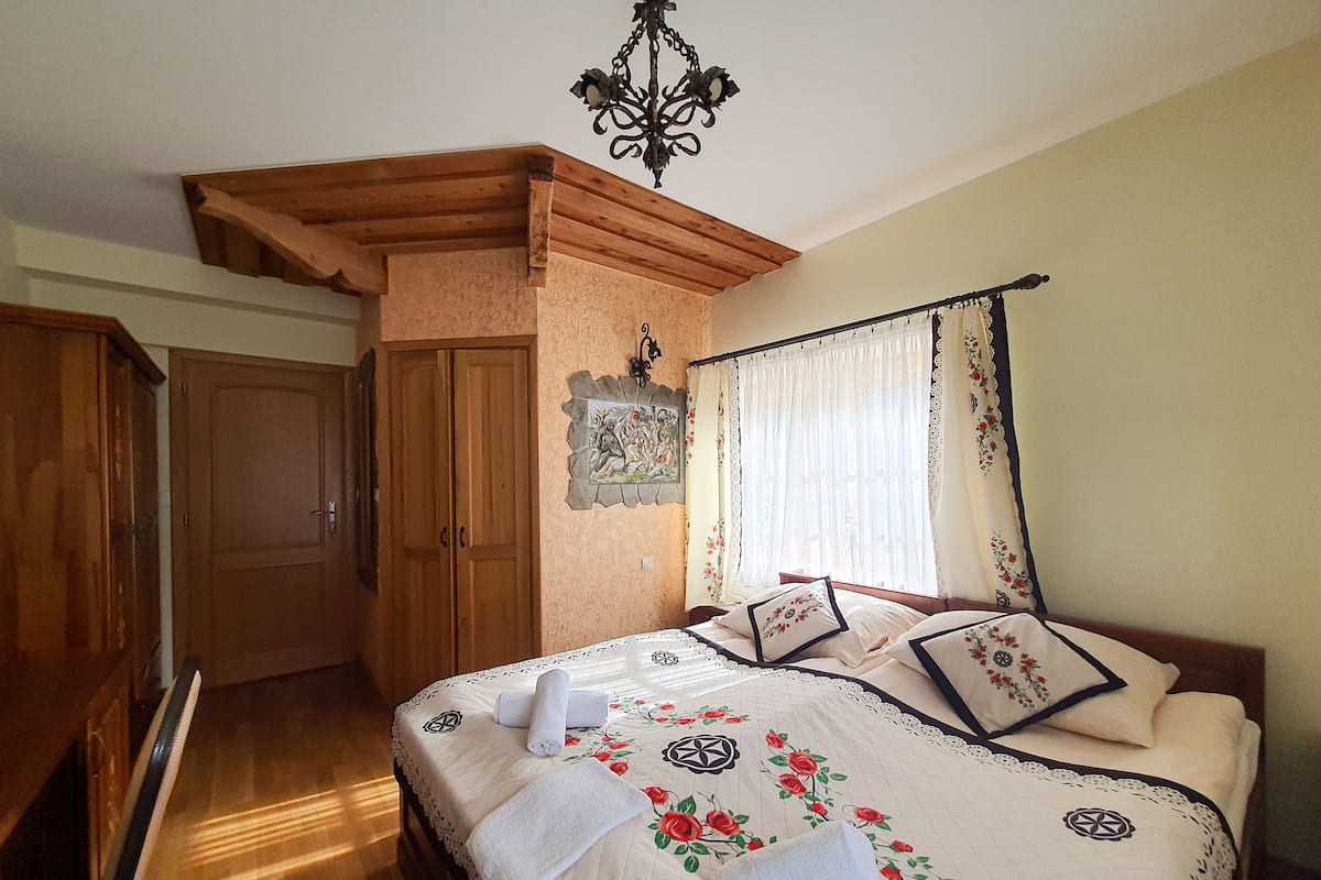 Un dormitorio con cama, armario de madera, puerta, candelabro y ventana con cortinas.