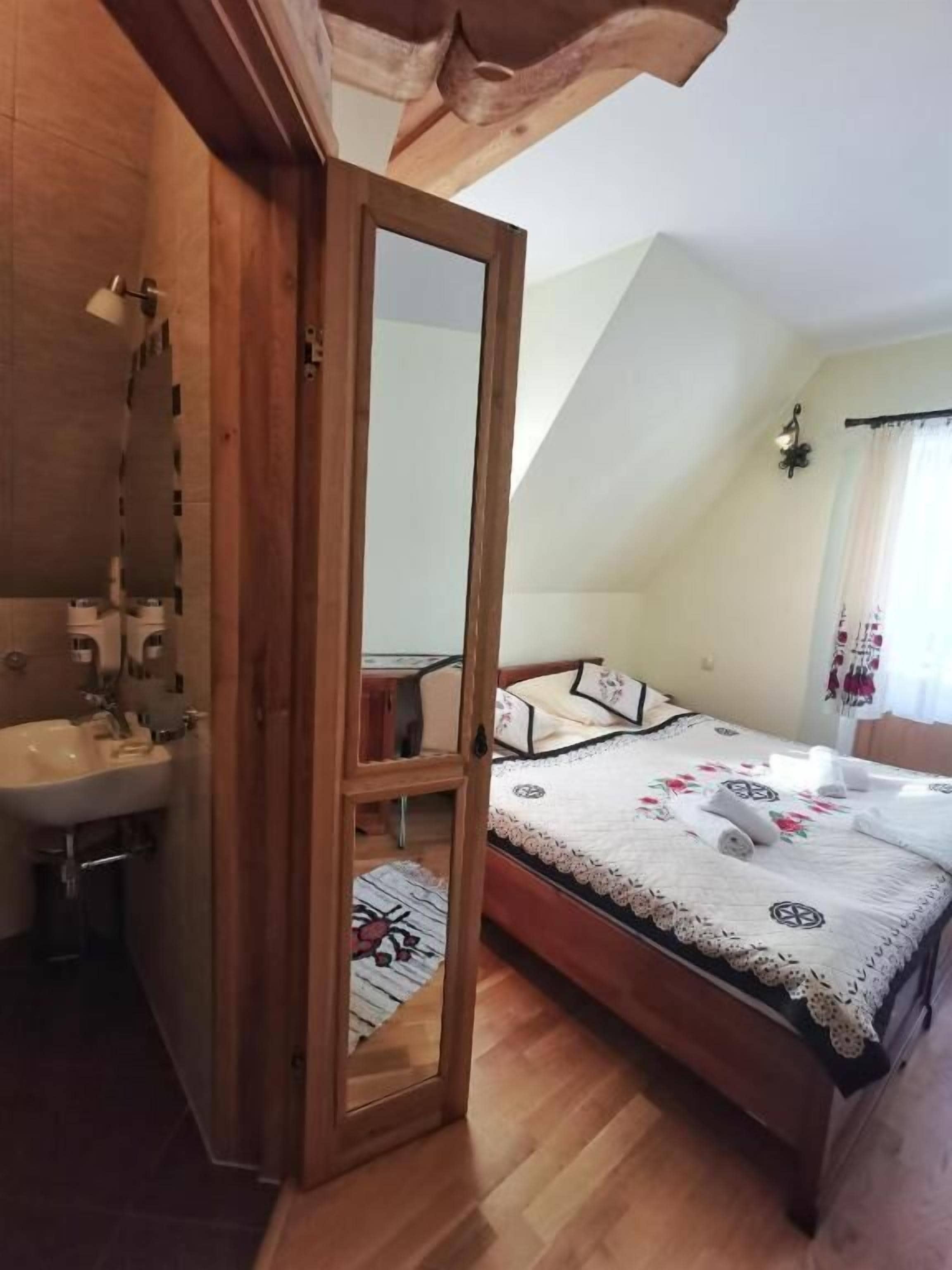 Un dormitorio con cama de madera, mesita de noche, espejo y ventana con cortinas.