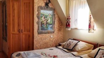 Un dormitorio con pared de piedra, vigas de madera en el techo, una cama con ropa de cama floral, un cuadro y una ventana con cortinas.