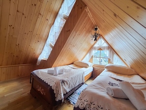 Une chambre mansardĂ©e en bois avec deux lits, un lustre et une vue sur les maisons par la fenĂȘtre.