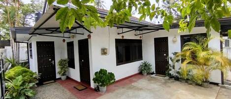 A white building with a covered porch, potted plants, and a concrete patio.